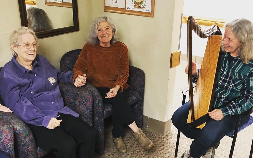 A Grace Center volunteer playing a miniature harp for participants 